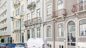 En hvid varevogn parkeret på en brostensbelagt gade foran en bygning med dekorative balkoner og store vinduer.