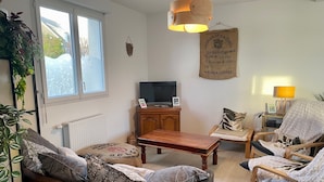 A cozy living room with a brown leather sofa, a wooden coffee table, a TV on a wooden cabinet, and a hanging light fixture. - Maison Neuve Livrée Début 2024 (Penmarc'h)