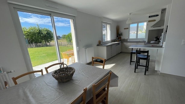 A bright kitchen with large windows, a dining area with a table and chairs, and a view of a green garden. - Maison Neuve Livrée Début 2024 (Penmarc'h)