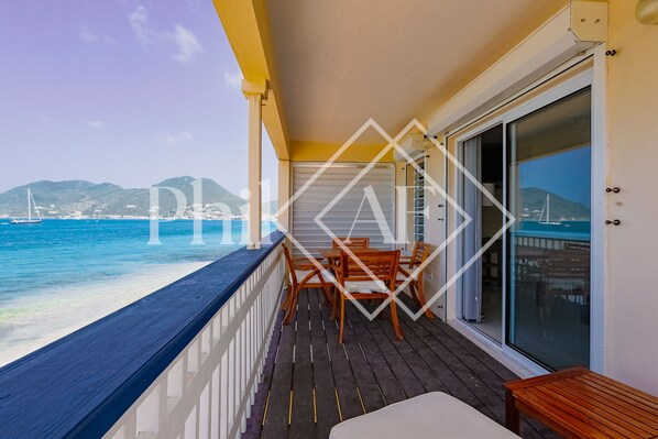 Ein Balkon mit Holztisch und -stühlen, Blick aufs Meer und ein Berg im Hintergrund.