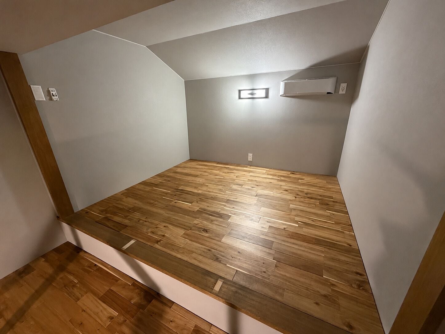 A room with a wooden floor, white walls, and a built-in shelf.