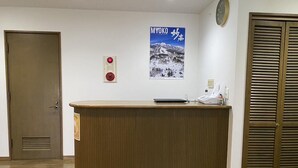 A reception desk with a wooden finish, a clock on the wall, and a poster of a snowy mountain scene. - Daiju Myoko (Myoko)