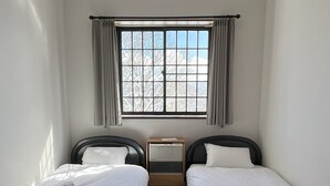 A room with two single beds, a window with curtains, a bedside table, and a radiator. - Daiju Myoko (Myoko)