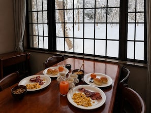 A dining table with breakfast plates, a glass of orange juice, and a view of a snowy landscape through a window. - Daiju Myoko (Myoko)