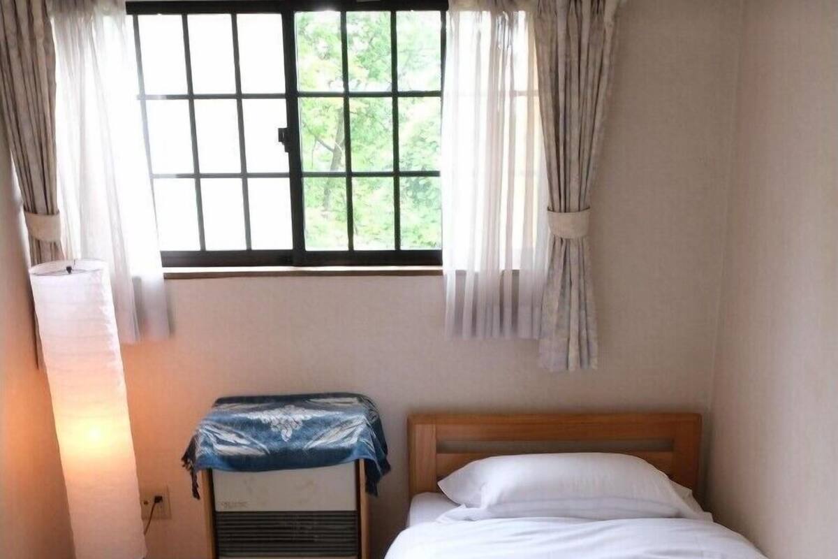 A single bed with white bedding, a bedside table with a lamp, and a window with curtains.