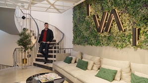 A modern interior with a spiral staircase, a green wall with illuminated letters, a beige sofa with green cushions, and a coffee table with magazines. - Feel Porto Firmeza Coworking Flat 4 1 (Porto)