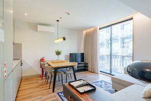 Un soggiorno moderno con pavimento in legno, un'area pranzo con tavolo e sedie, un divano, una TV e un'ampia finestra con tende.