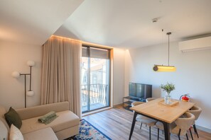 Una camera d'albergo moderna con divano, tavolo da pranzo, televisione e balcone con tende.