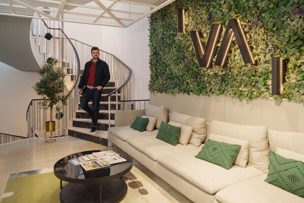 A modern interior with a spiral staircase, a green wall with 'I.V.AI' illuminated letters, a beige sofa with green cushions, and a coffee table with magazines. - Feel Porto Firmeza Coworking Flat 4 2 (Porto)
