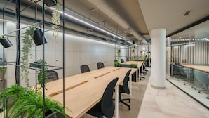 Un espacio de oficina moderno con mesas largas, sillas de oficina negras y plantas en macetas.