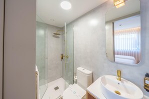 A modern bathroom with a glass-enclosed shower, a white sink with gold fixtures, and a large mirror reflecting the room. - Feel Porto Firmeza Coworking Flat 4 4 (Porto)