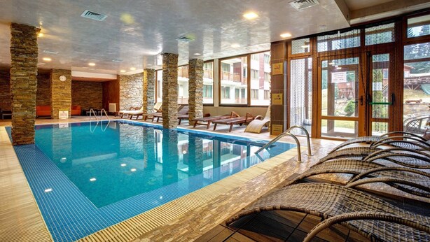 Une piscine intérieure dotée de piliers en pierre, de chaises longues et offrant une vue sur l’extérieur.