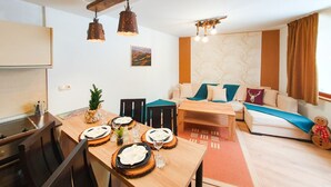 Un salon moderne avec un coin repas, comprenant une table en bois dressée pour quatre personnes, un canapé avec des coussins et une décoration murale.