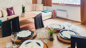 Un salon moderne avec un canapé, une table à manger pour quatre personnes et une fenêtre donnant sur un immeuble et des arbres.