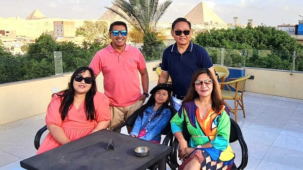 A group of people seated at a table on a rooftop terrace with a view of pyramids in the background. - Regent Pyramids View (Giza)