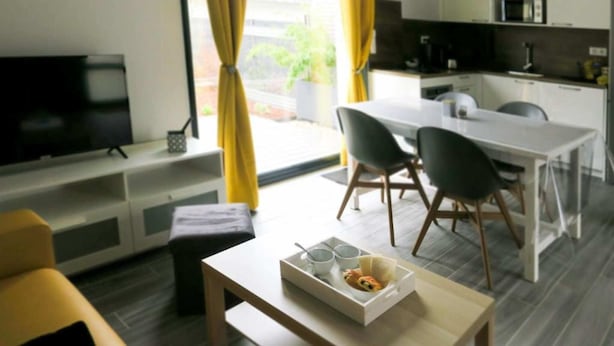 A modern living room with a TV, seating, and a dining area with chairs and a table.