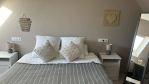 A bedroom with a bed, two nightstands, a wall clock, a mirror, and a window.