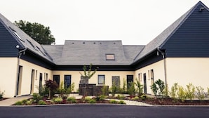 A modern building with a symmetrical facade, a central courtyard with a stone feature, and a sloped roof.