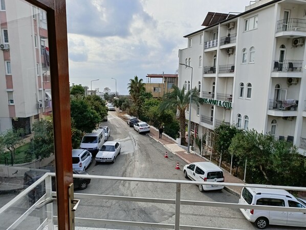 Vista de la calle con coches estacionados, una furgoneta blanca y edificios de varios pisos con balcones.
