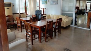 Un comedor con una mesa y sillas de madera, un sofá y un amplio ventanal con cortinas.