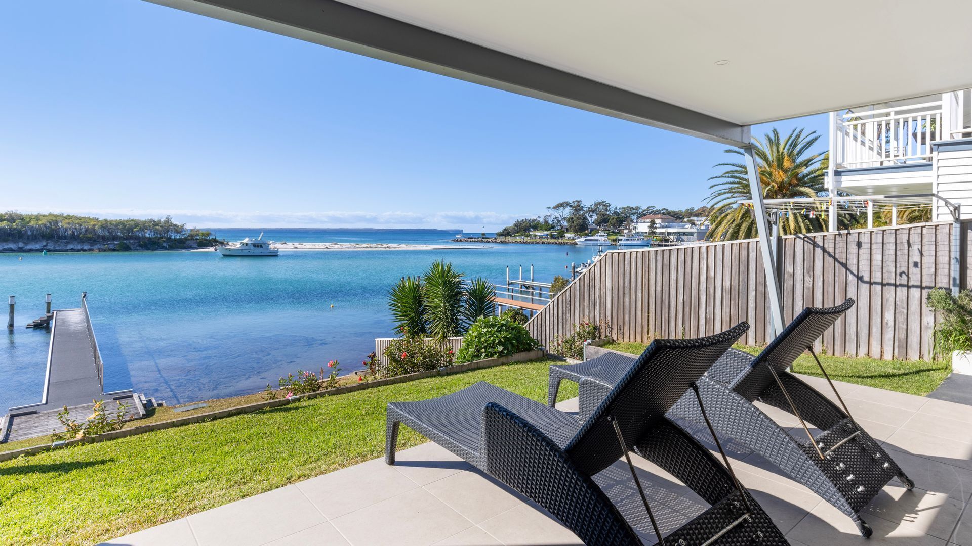Ein Balkon mit Gartenmöbeln, der auf eine Marina und das klare Meer blickt.