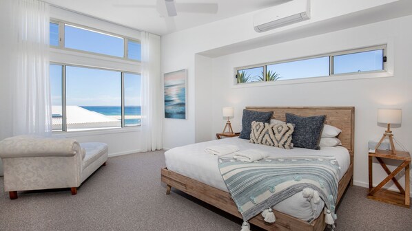 A bedroom with a large bed, two bedside tables, a chair, and a view of the beach.