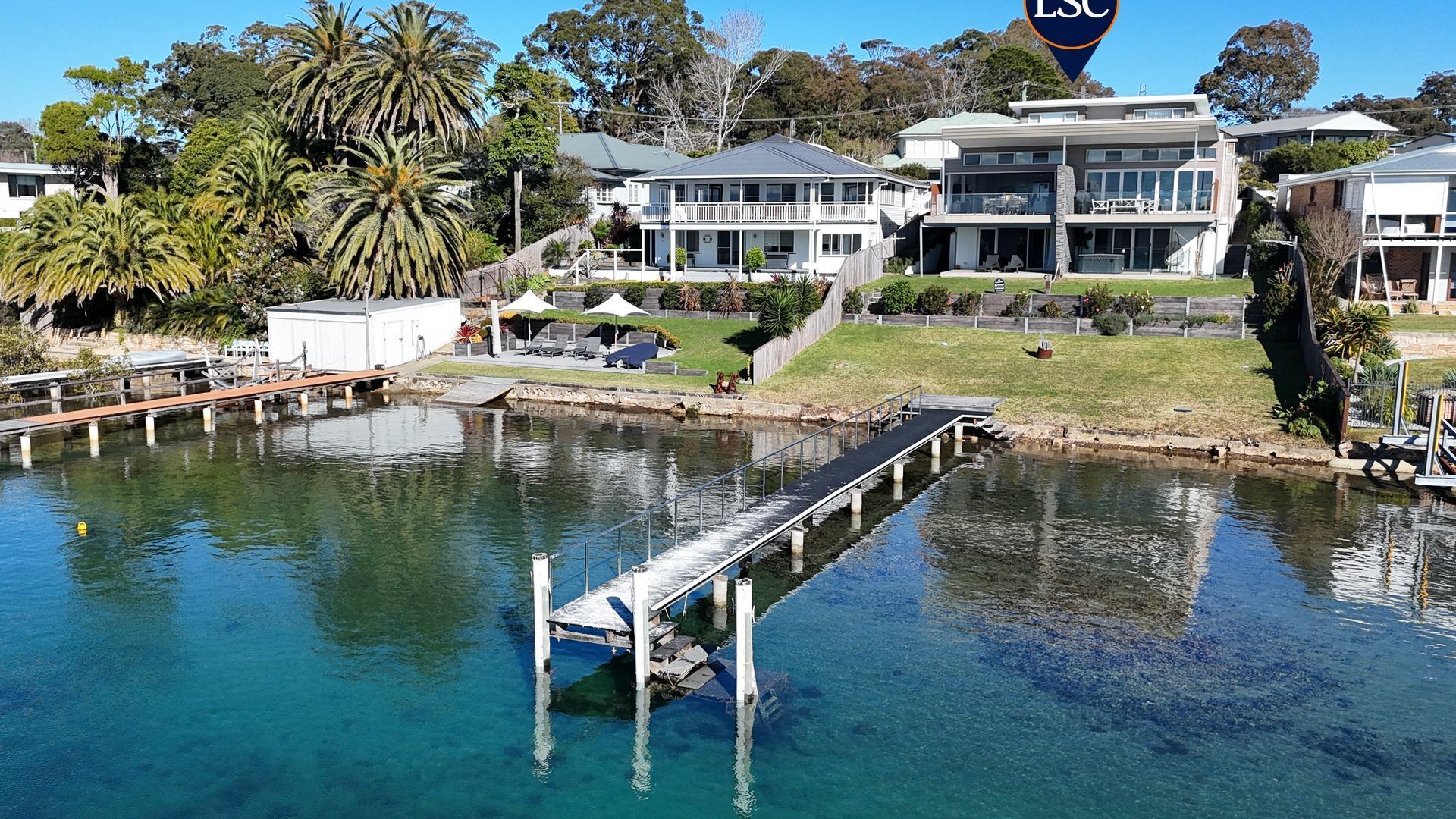 A waterfront property with a dock, a large house with multiple levels, and lush greenery.