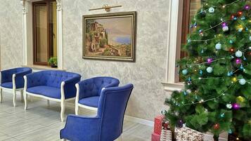 A lobby with a Christmas tree, blue upholstered chairs, and a framed painting on the wall.