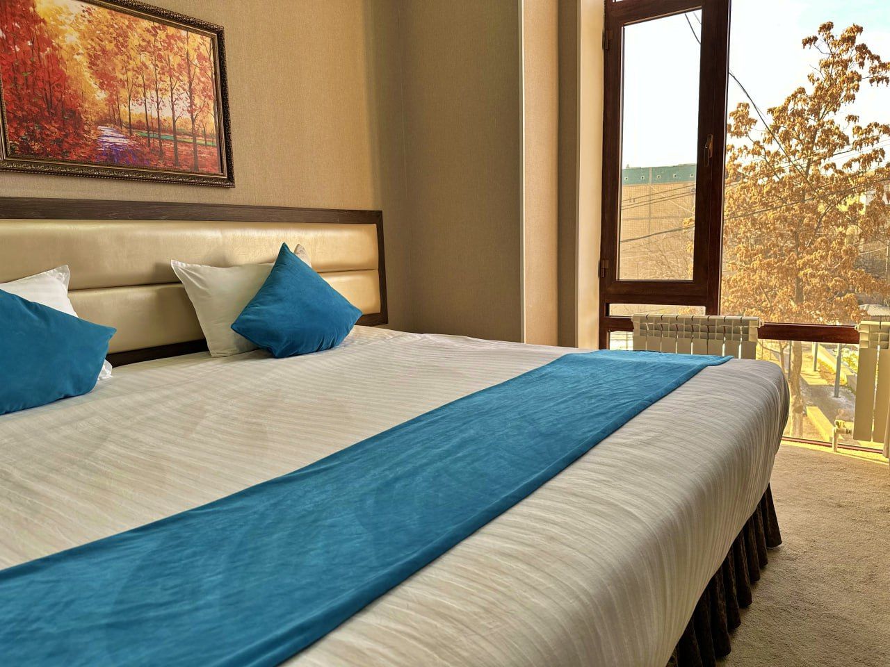Une chambre d’hôtel avec un grand lit, une tête de lit, une fenêtre donnant sur des arbres et un tableau au mur.
