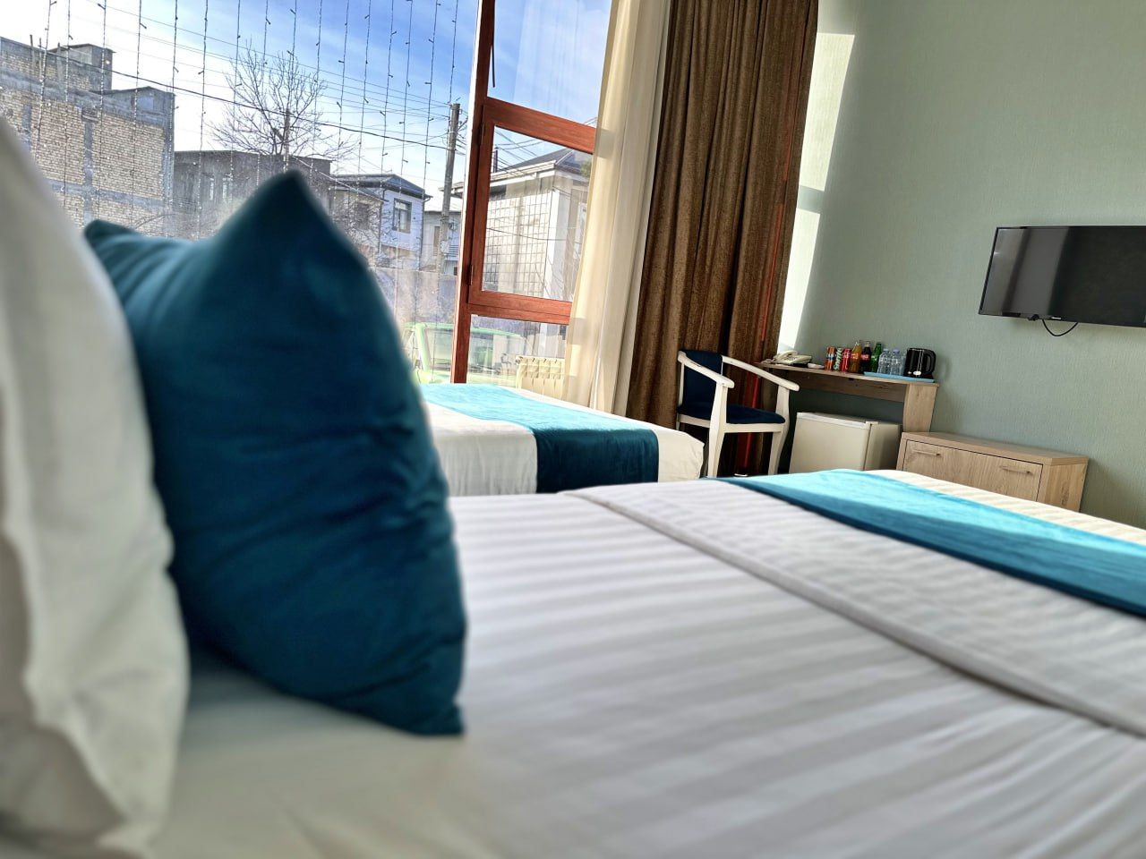 A hotel room with two beds, a desk with a chair, a television, and a window with a view of buildings.