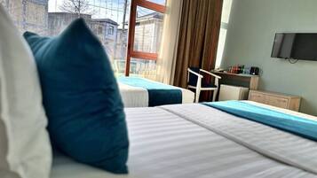 A hotel room with two beds, a desk with a chair, a television, and a window with a view of buildings.