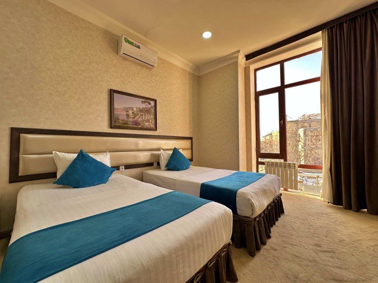 A hotel room with two beds, a large window, and a view of the city.