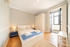 A bedroom with a bed, bedside tables, a wardrobe, a small table, and a view of the outside. - GuestReady - Splendid stay with balcony in Lisbon (Lisbon)