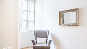 A room with a grey armchair, a mirror with an ornate frame, and a window with curtains.