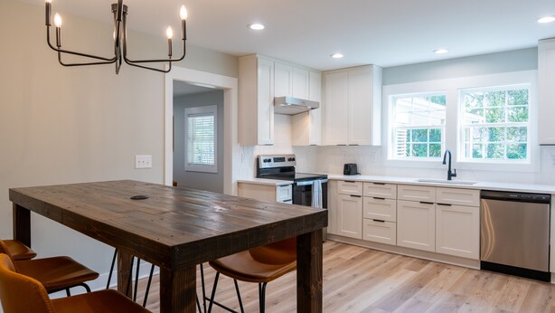 A modern kitchen with white cabinets, a wooden dining table, and a built-in oven.