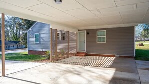 A covered porch with a small shed, a concrete patio, and a door leading to a house.