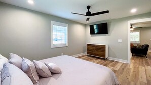 A bedroom with a bed, a ceiling fan, a TV mounted on the wall, and a window with blinds.
