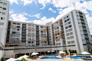 Un hotel de varios pisos con piscina en la azotea, zona de estar exterior y un cielo azul despejado.