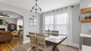 A dining area with a wooden table, chairs, and a chandelier. There is a fireplace, a television, and framed pictures on the wall. - Swamp Rabbit | Furman | Bikes | Pass | Fenced | EV (Greenville)