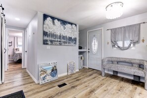 Ein Zimmer mit Holzboden, einer Bank, einer Tür mit dekorativem Glasfenster und einem großen Gemälde an der Wand.