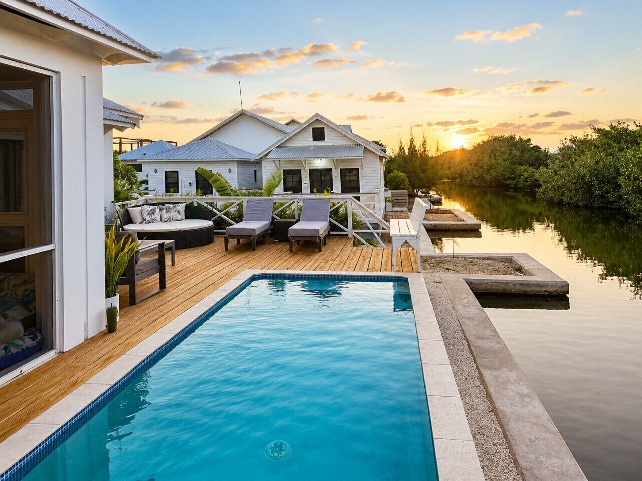 A swimming pool with lounge chairs and a wooden deck, surrounded by a house and a calm body of water.