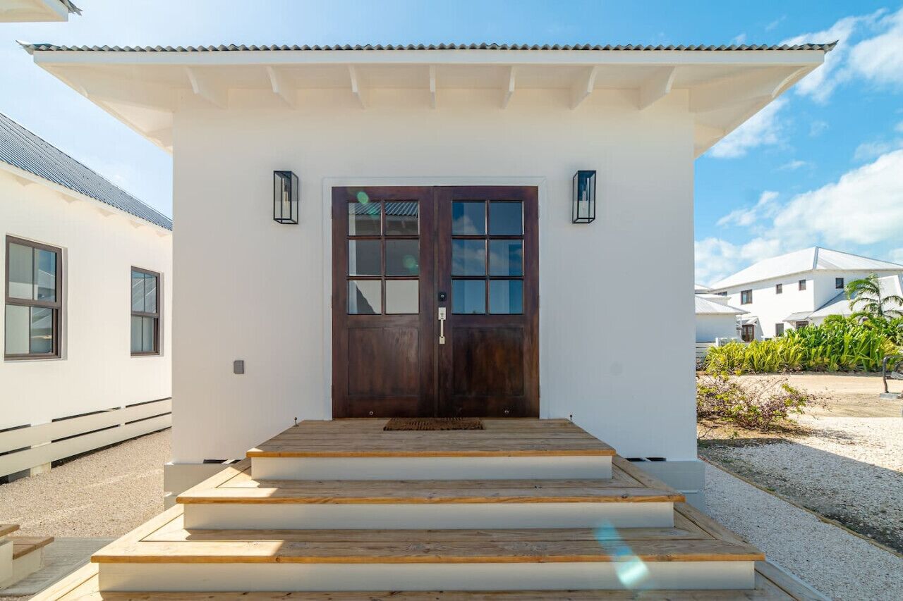 A white building with a dark wooden door, steps leading up to the entrance, and a small porch area.