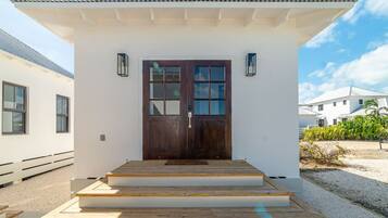 A white building with a dark wooden door, steps leading up to the entrance, and a small porch area.