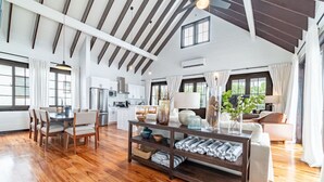 A spacious living area with wooden flooring, a dining table with chairs, a sofa, and a coffee table with decorative items.