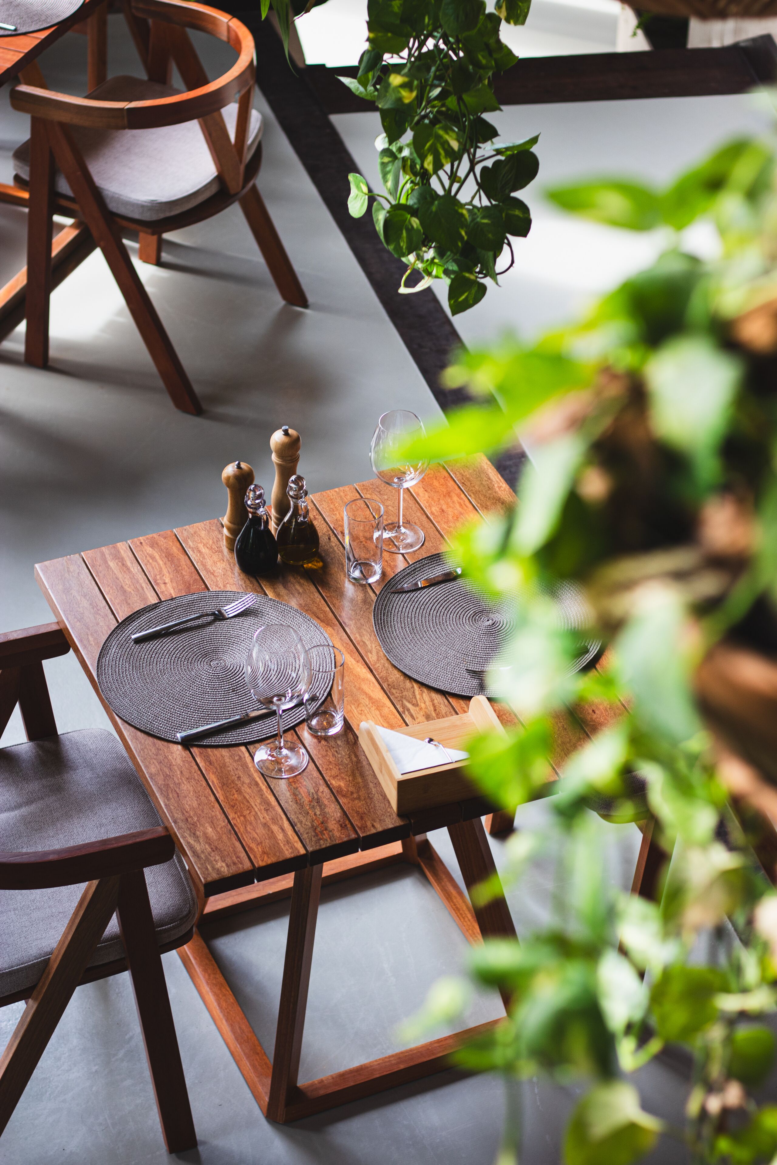 A wooden dining table set with placemats, cutlery, and wine glasses, surrounded by chairs.