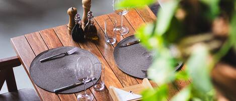 A wooden dining table set with placemats, cutlery, and wine glasses, surrounded by chairs.