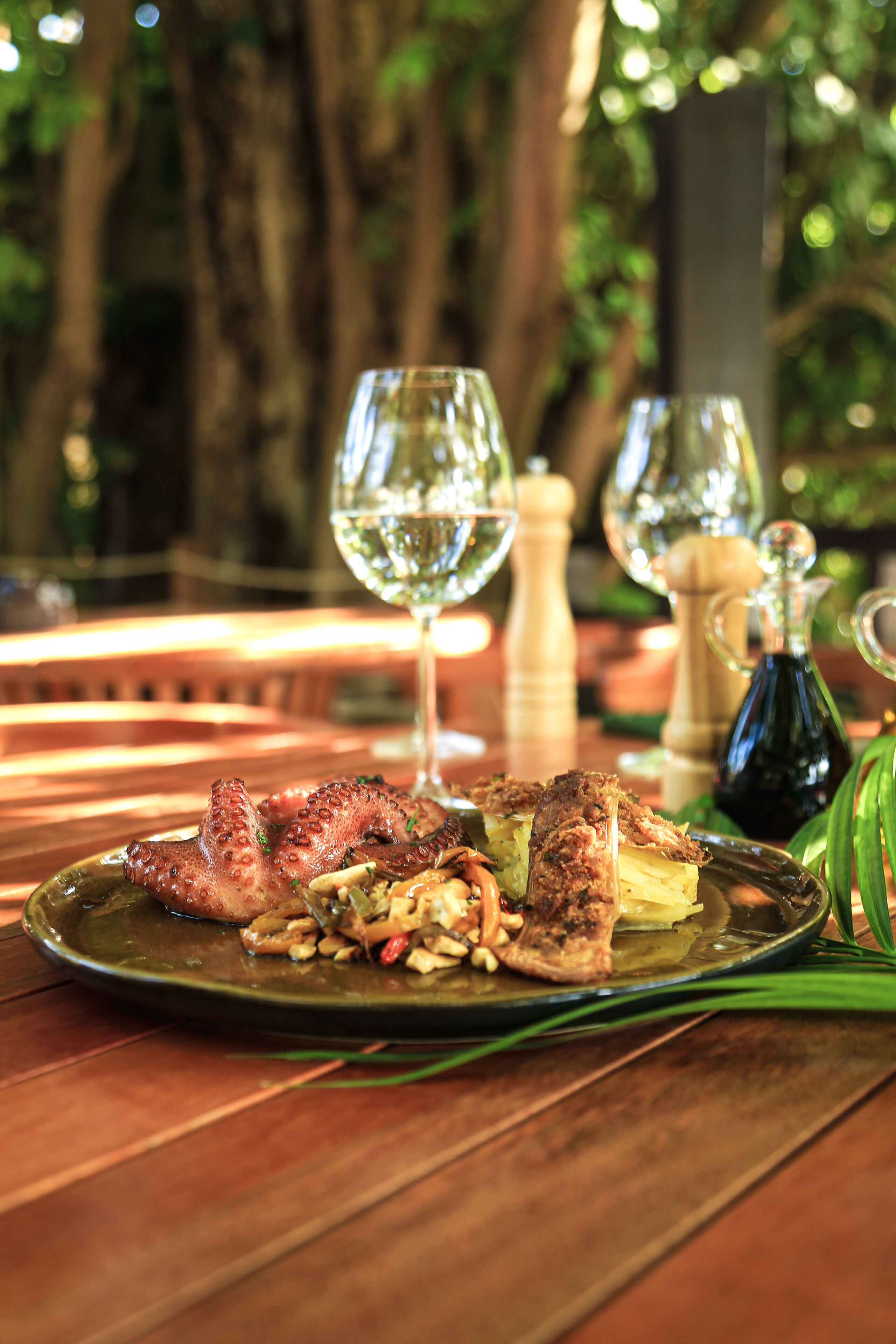 A dining table with a plate of food, two wine glasses, and a salt and pepper shaker.