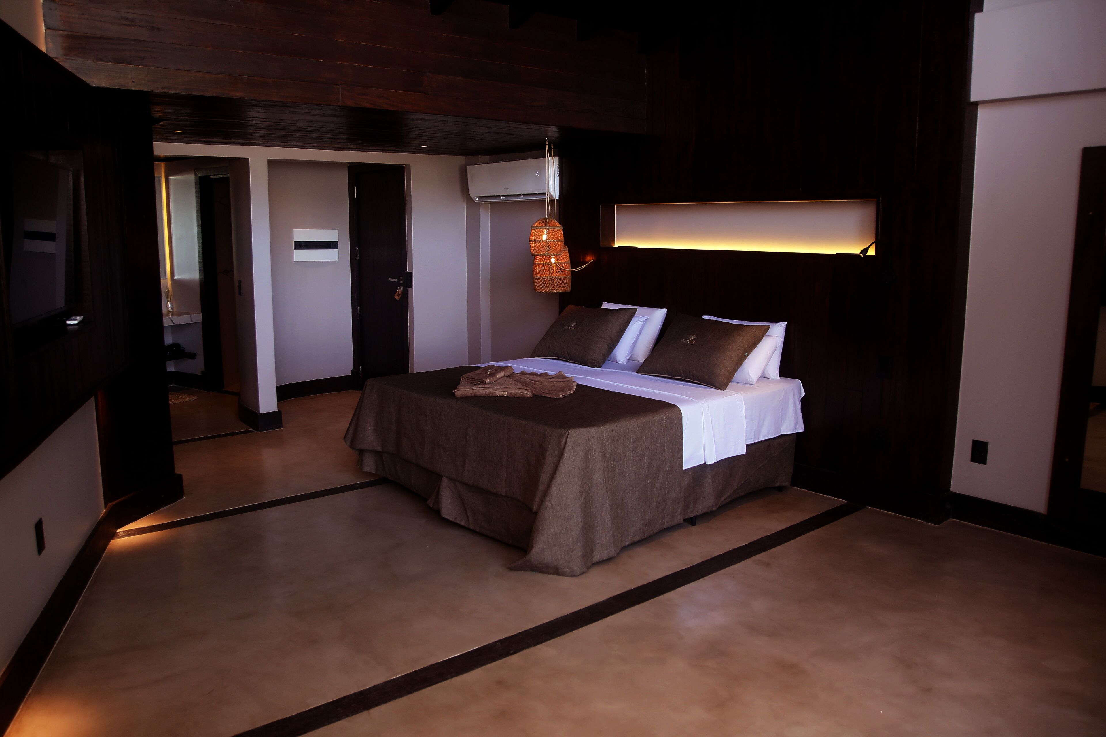 A modern hotel room with a large bed, a bedside table, and a hanging light fixture.