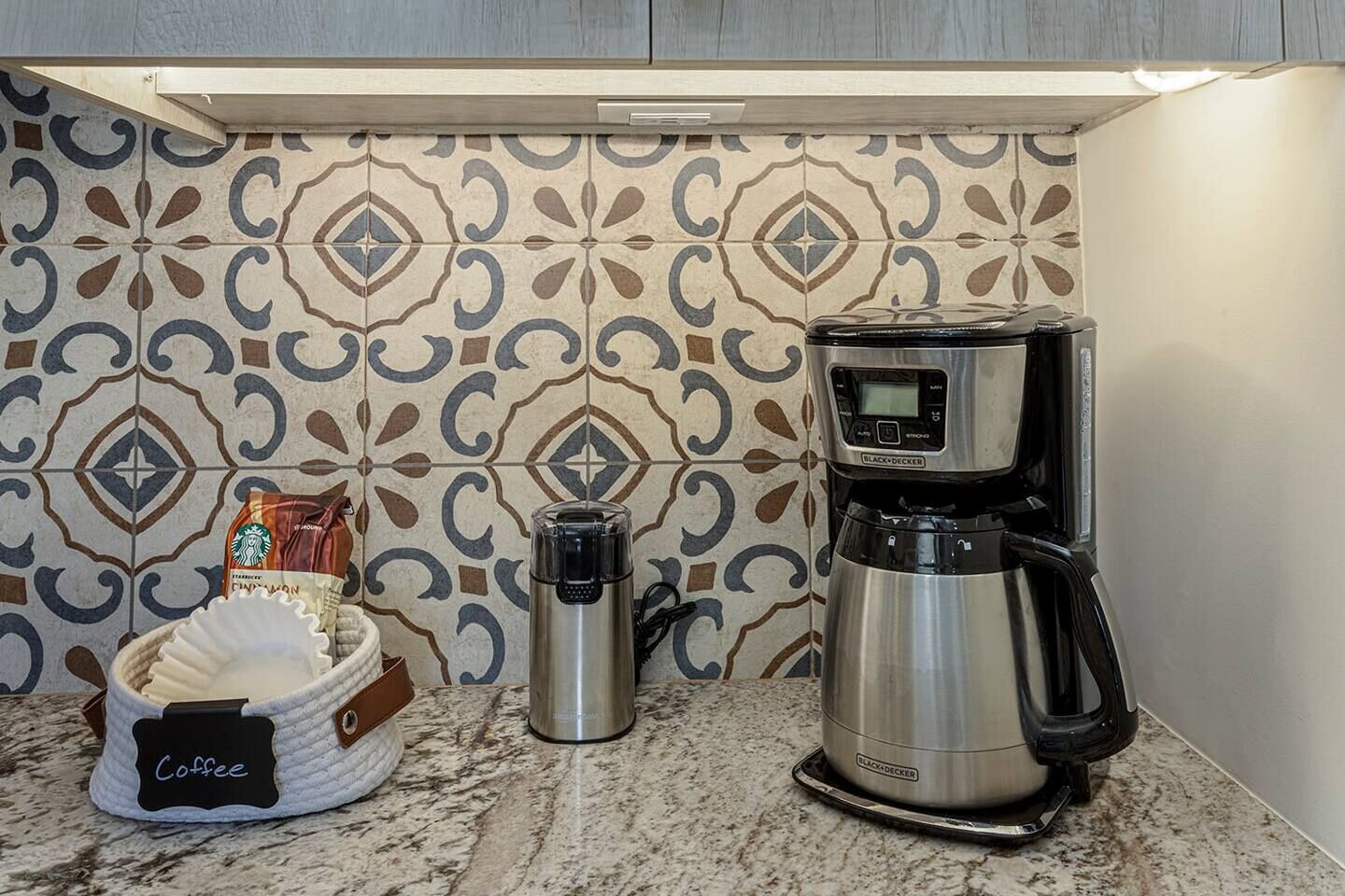 A coffee maker, a thermos, and a coffee bag on a marble countertop.