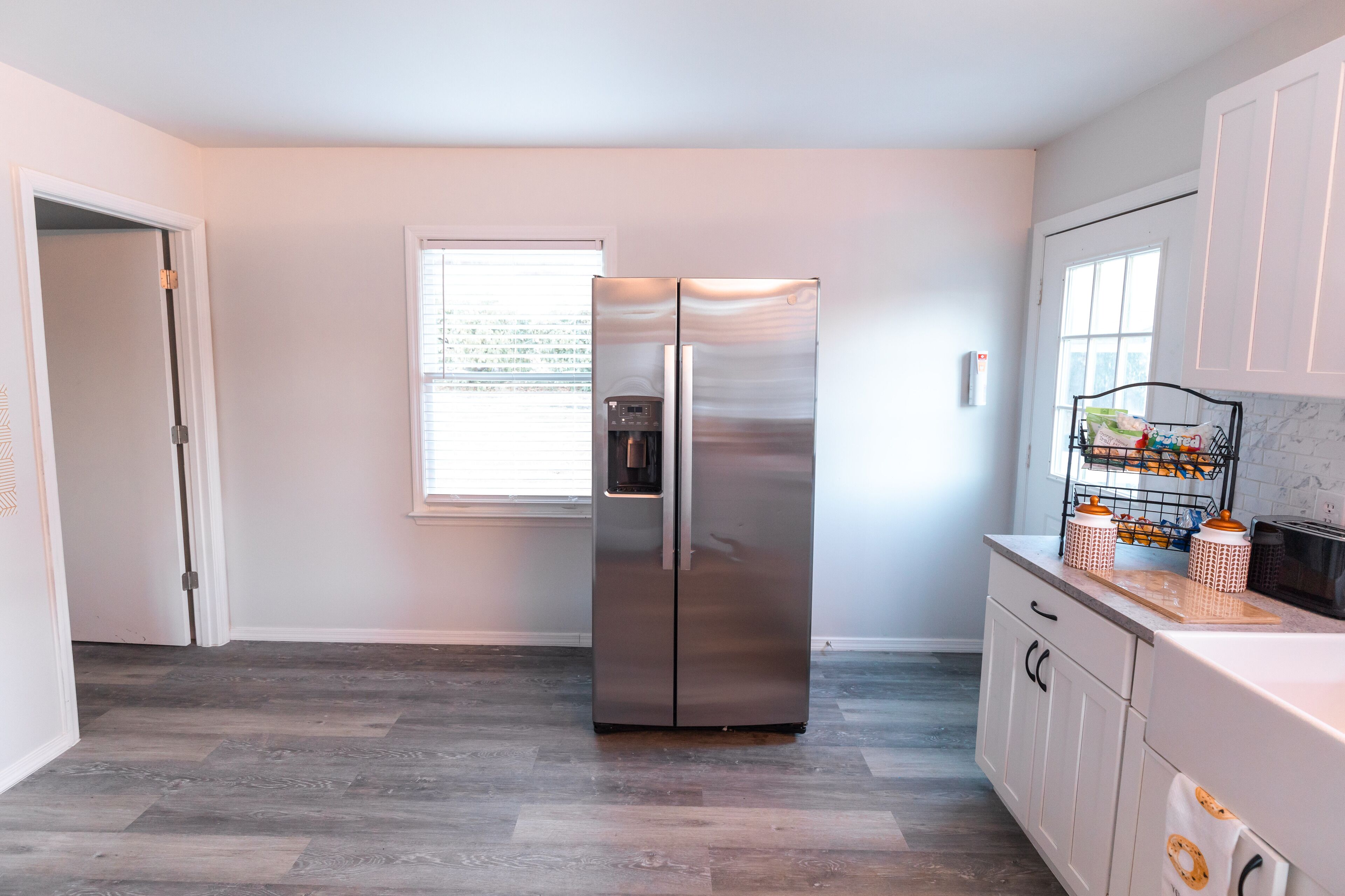 A modern kitchen with a stainless steel refrigerator, a window with blinds, and a countertop with kitchenware.